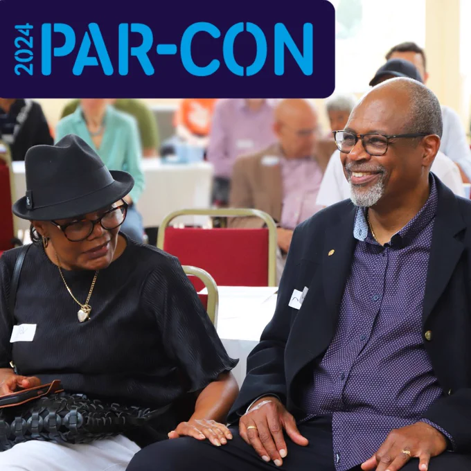 Two attendees smiling and engaging in a conversation at the 2024 PAR-CON conference, surrounded by other participants in a brightly lit room.