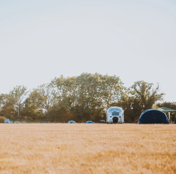 A silver Airstream campervan and tents in a golden field at Coxhill Camping, Shepherdswell, Kent.
