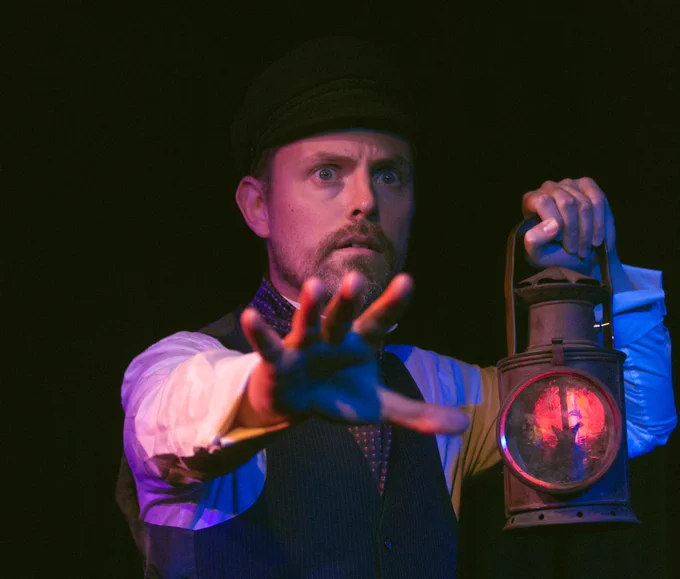 Tim Larkfield performs in The Signalman, holding his hand up in warning and holding a Victorian lantern in his other hand. Image credit: Elee Nova.