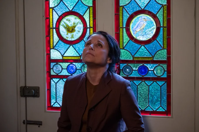 Still from Tuesday showing woman leaning against a stained glass door and looking bereft.