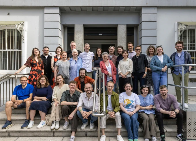 A group shot on a bright sunny day of (almost) everyone involved in The House taken on the steps outside the rehearsal room