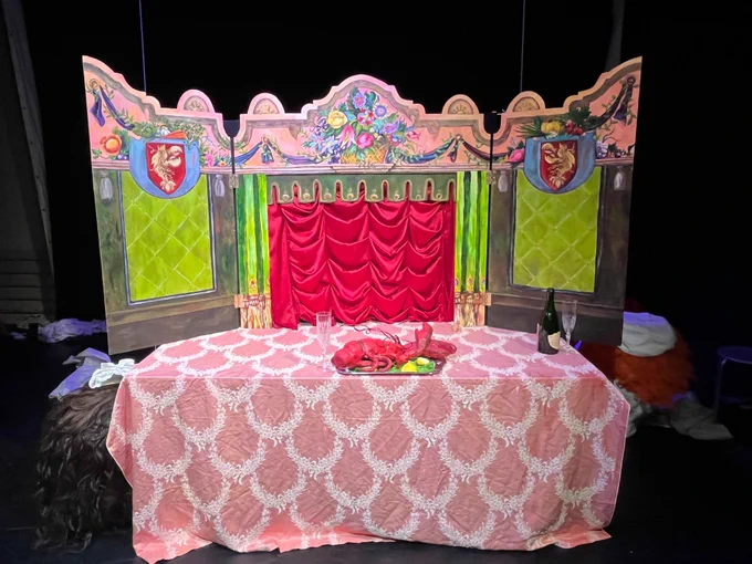 On a stage, a puppetry table with bright colors. a model lobster is on the center of the table.