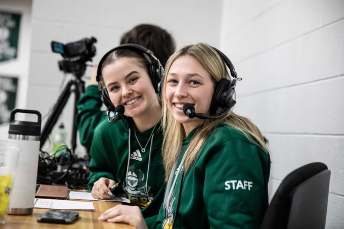 Two student staff with headsets, smiling for the camera.