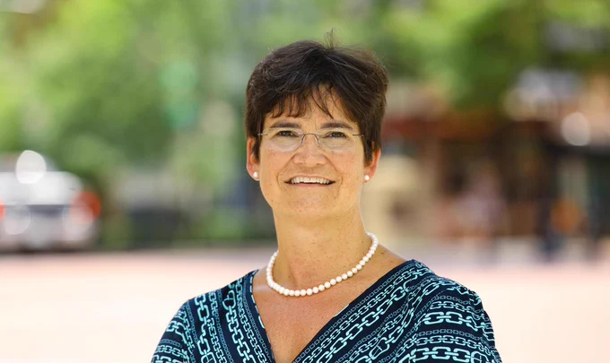 White woman in glasses and blue printed top stands outdoors.