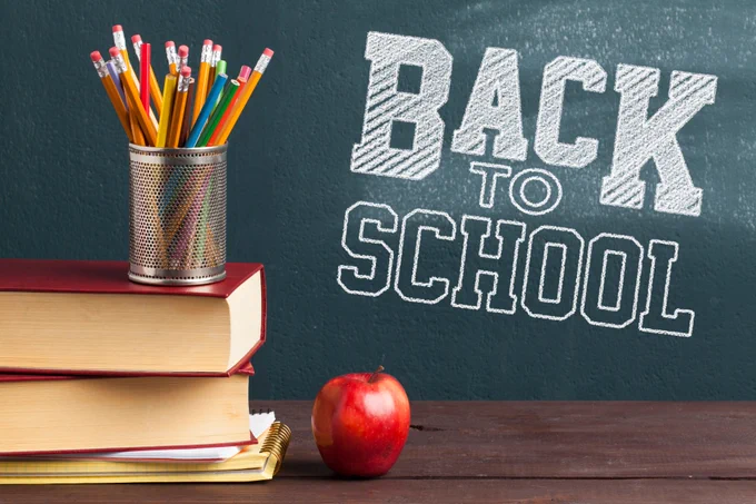 A stack of books, an apple, and a container of pencils. The words "back to school" are emphasized on a blackboard behind these objects.