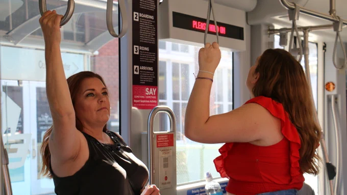Two women cooling off and holding on the the overhead straps on board the OKC streetcar.