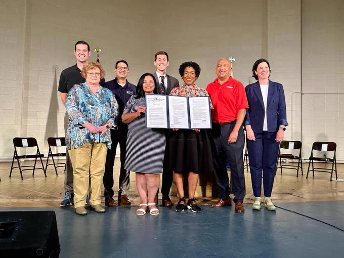 Lt governor Stratton stands with a group of people on stage, holding the executive order establishing the Multi-Sector Plan for Aging at the signing event