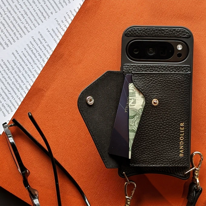 Obsidian Pixel 9 in a Bandolier phone case with money and a card in the pocket attached. The case is next to a pair of glasses.