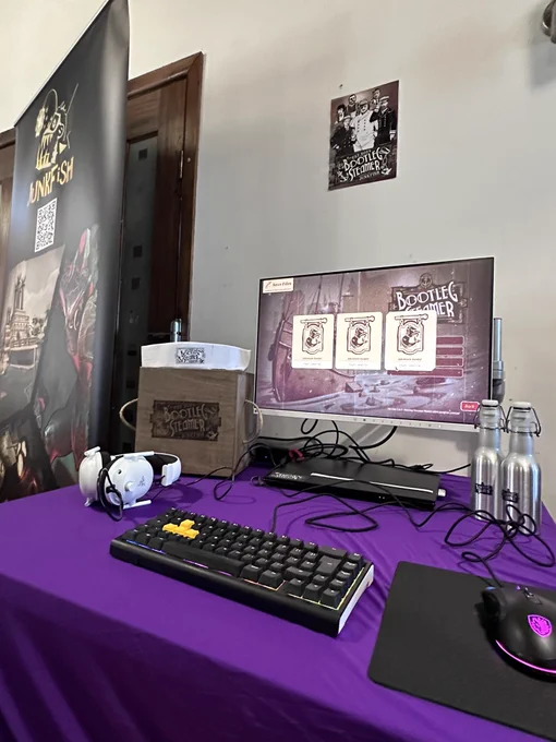 A computer desk set up with purple covering. A computer with the game bootleg steamer is on the screen. It is surrounded by Bootleg Steamer merch.