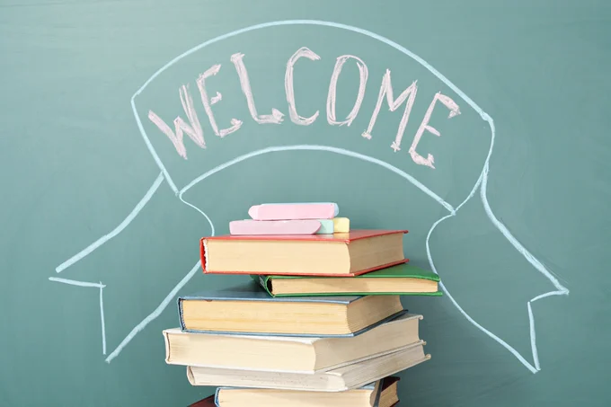 The word 'Welcome' above a stack of books, on a turquoise blue background. 