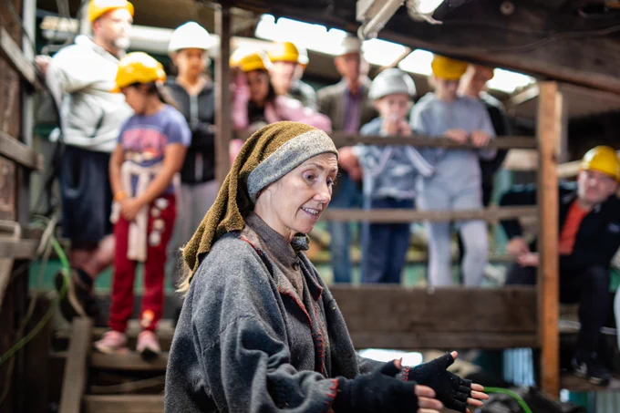 a pit brow lass in the museum's screens building speaking to visitors who are wearing hard hats