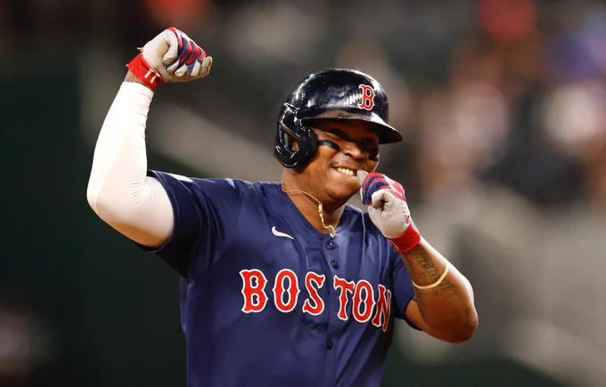 Rafael Devers pumps his fist as he rounds the bases. He wears an alternate blue Red Sox uniform with red and white lettering. 