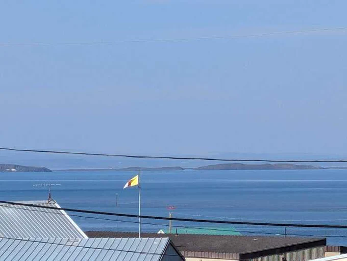 A picture of the official flag of Nunavut with the horizon of the Arctic Ocean in the background. 