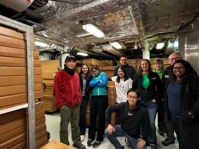Expedition 403 scientists gather for a photo in the reefer with all the cores collected during the expedition in boxes around them.