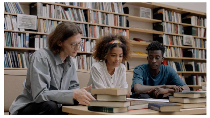 Three people at a table in the library looking at books
