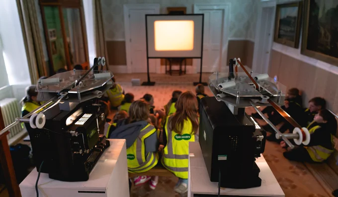 Two 16mm looped projects create an abstract image on a standup screen, watched on by school pupils.