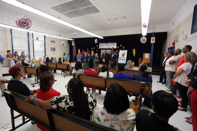 A room filled with people sitting down, looking at a stage where people are standing and talking