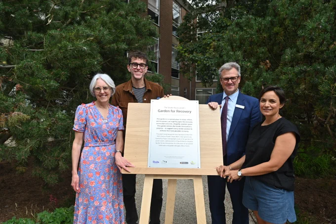 Four people stood outside around a plaque that reads 'Garden for Recovery.' 