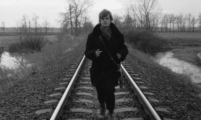 Still from Werckmeister Harmonies showing man running down a train track.