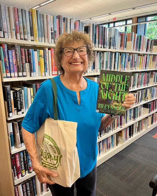 Photo of a summer reading prize winner holding up a book and her Check Out Your Happy tote bag.