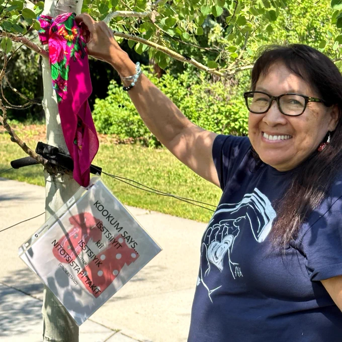 Kainai (Blackfoot) Elder Wanda First Rider displaying her kokum scarf on a tree outside the University of Calgary Education Tower. The scarf is a call to understand the issues surrounding missing and murdered Indigenous women and girls.