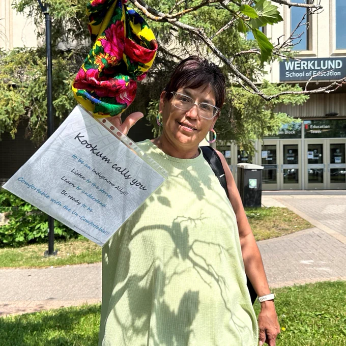 Angela Bear Chief displaying her kokum scarf on a tree outside the Education Classroom Block. The scarf is a call for people to be an Indigenous ally.
