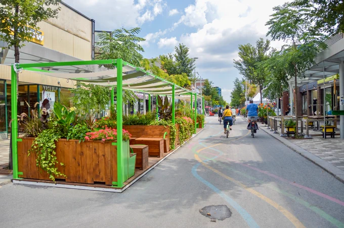 People walk, sit, and dine along a pedestrianized street in Montreal. It is lined with trees, planter boxes, terraces, and benches.