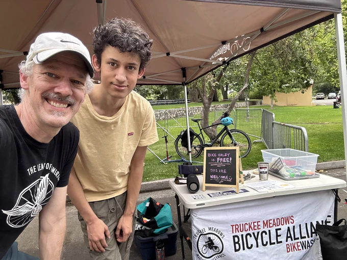 Two dudes smiling in front of a bike valet booth at an outdoor event