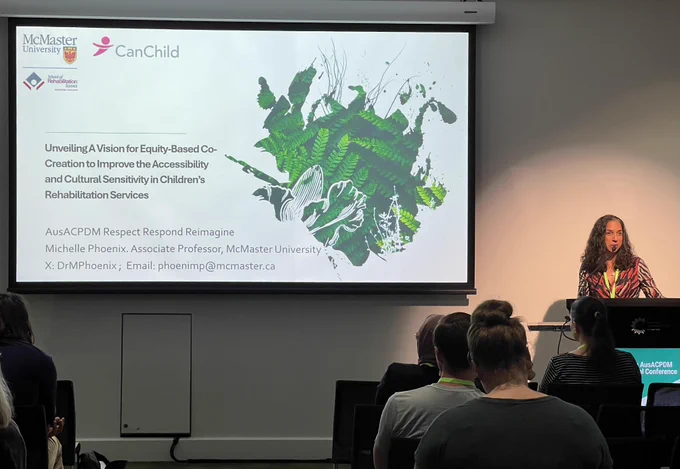 Michelle Phoenix at podium with slides showing title "Unveiling a vision for equity-based co-creation to improve the accessibility of children's rehabilitation services" 