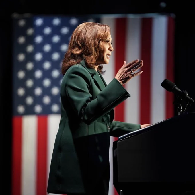 Vice President Kamala Harris speaking at a podium with a large American flag in the background.