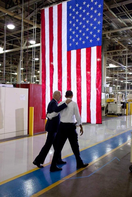 President Biden and former President Barack Obama walk together in front of an American flag.