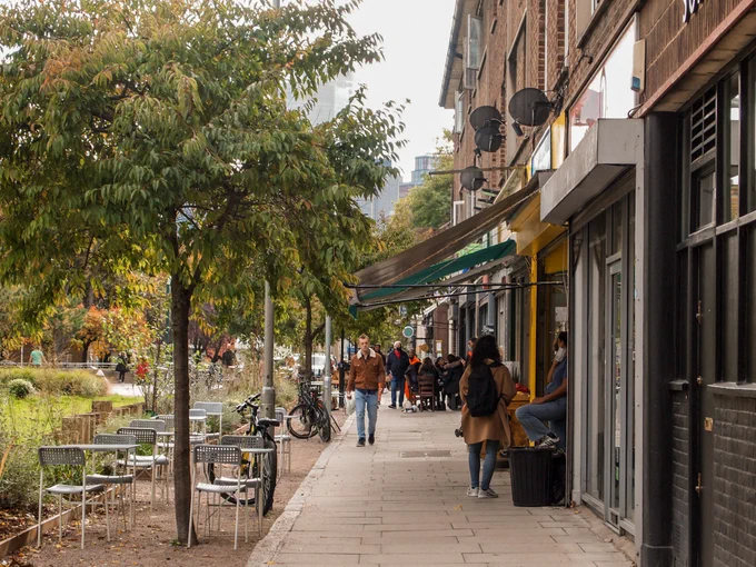A city retail street scene where trees have been added into the kerbside space to create a setting for a cafe. 