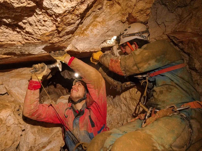 Two cavers in the cave, securing one of the walls.