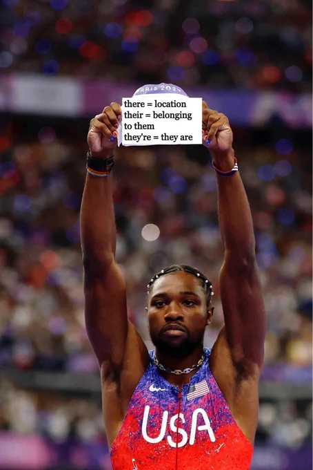Noah Lyles holding up a sign that says 
"there = location
their = belonging 
to them
they're = they are"