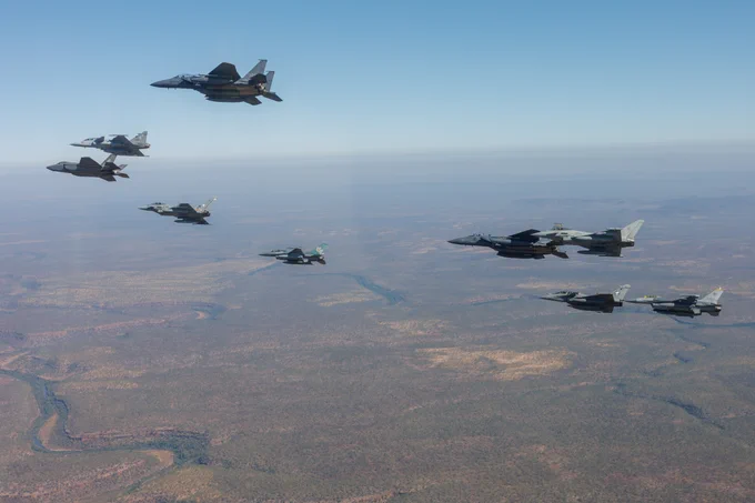Nine aircraft from different nations flying together, with land visible below.