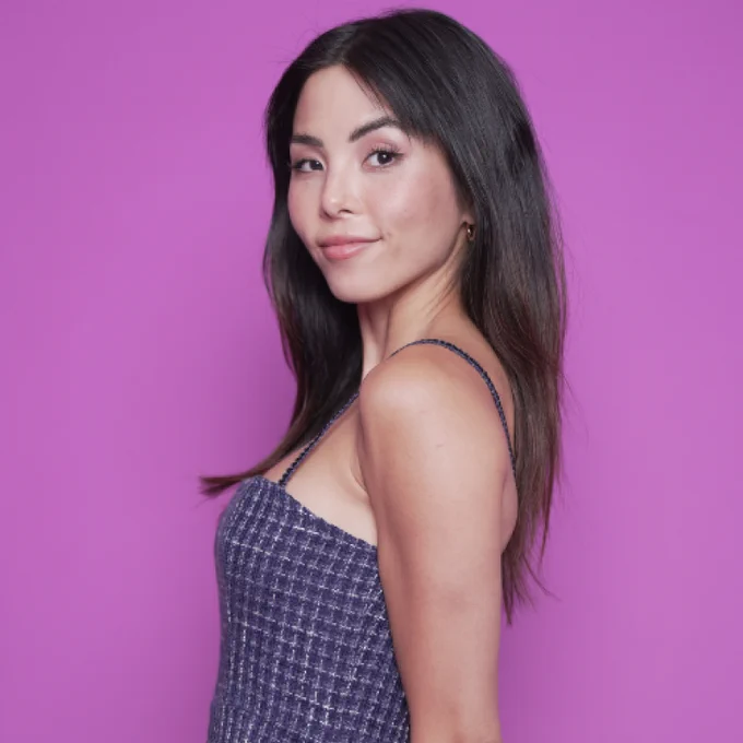 A photo of Anna Akana wearing a purple dress standing in front of a purple background