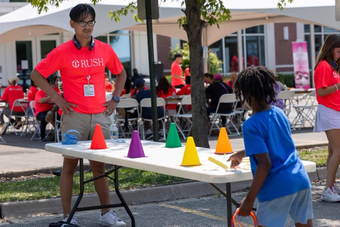 A Rush University student standing by a table with colorful cones, playing a game with a child. 