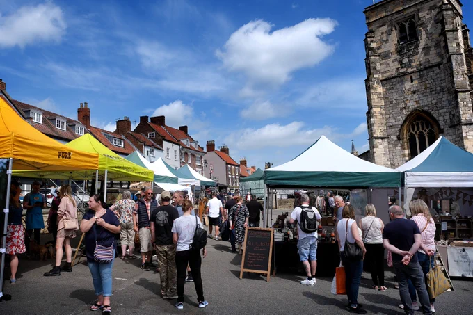 Malton Monthly Food Market in the Market Place in the area in front of St Michael's Church. Stall holders with artisan products and visitors shopping.