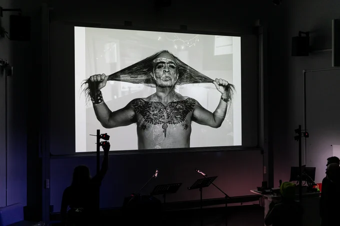 Photo of a monitor displaying a b&w image of Guillermo Gómez-Peña