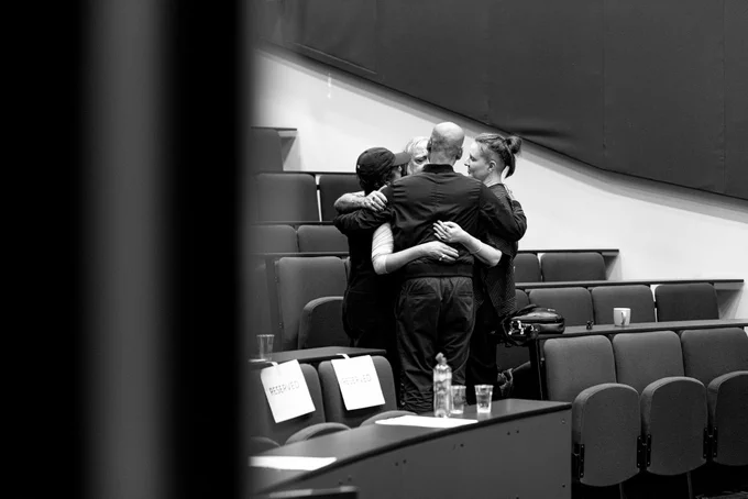 B&w photo of a group hug inside a lecture theatre
