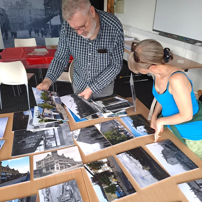 Two people discussing old photographs of Colne laid out on a table 