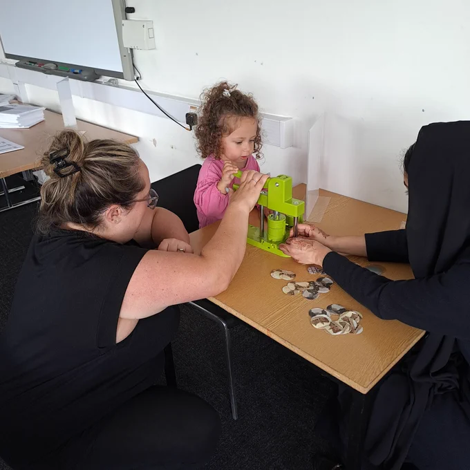 A young child and two adults making badges 