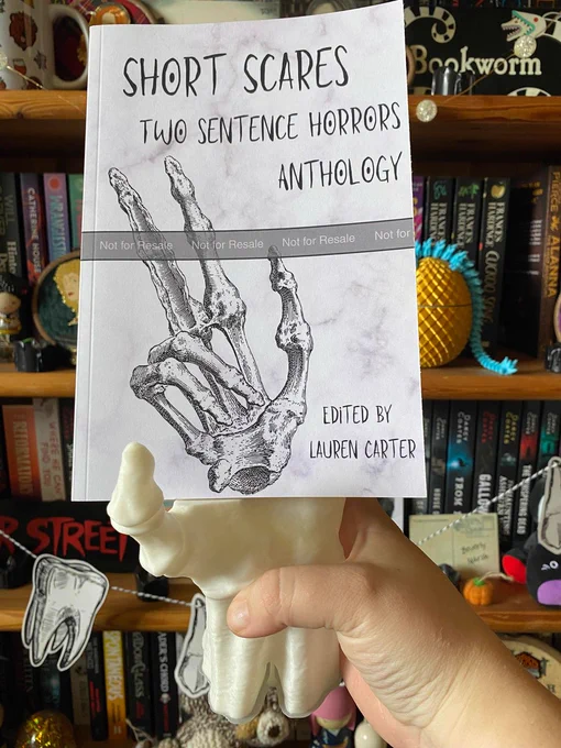 Front cover of SHORT SCARES
Two sentence Horrors anthology
Edited by Lauren Carter
(a skeleton hand is on the front, giving a cool peace sign)