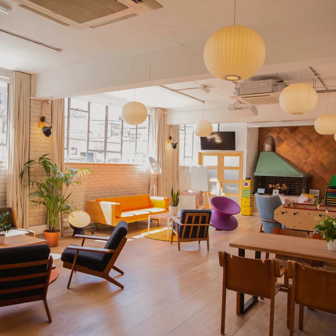 Interior space - light and airy with big windows, seating areas with chairs and couches, a stage with a fireplace, and table and chairs.