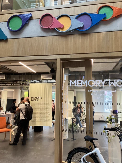 Entrance to the UCL East Urban Room with 'Memory Work' etched into the glass door and people inside looking at the exhibition