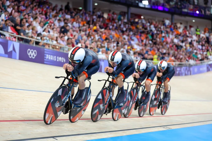Team GB's team pursuit race around the velodrome with the crowd in the background. All four of them bent low over their handlebars