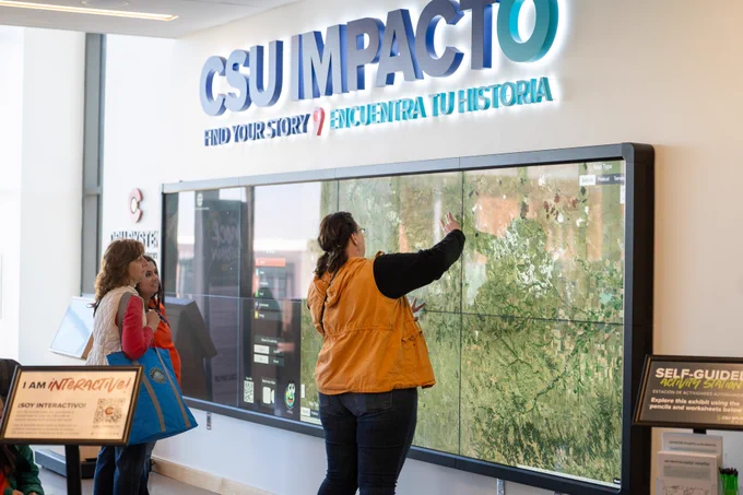 One person interacting with a large map on a large TV display. Two people are standing to the left.
