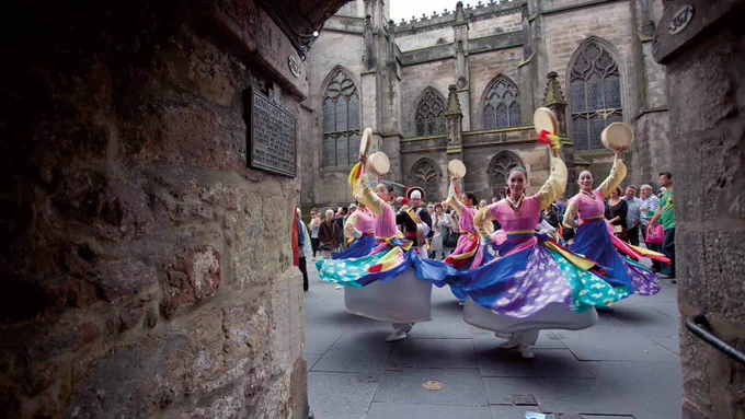 View of dancers from a close (alley) on an historic street in the city of Edinburgh, Scotland. The dancers are wearing colourful traditional dress from Asia and are captured mid-twirl as they move down past.