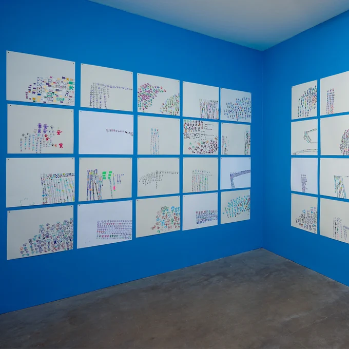 Angled view of the installation Roland Young at Studio Voltaire. Unframed drawings are arranged in a grid formation on a blue wall.