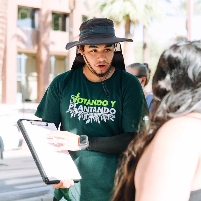 Canvasser/volunteer registering voter, wearing "Votando y Plantando" shirt